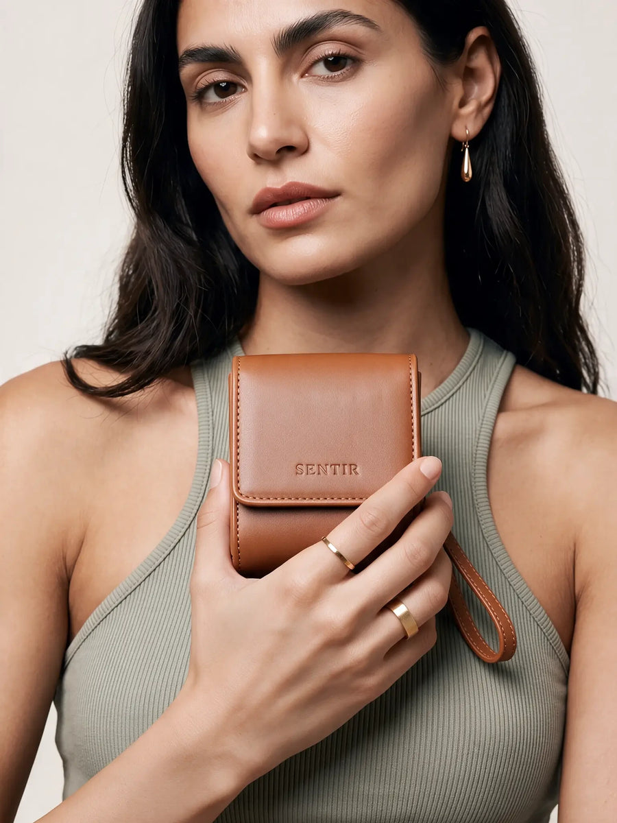 Woman holding the brown vegan leather Sentir travel pouch against her top, showing how compact it is