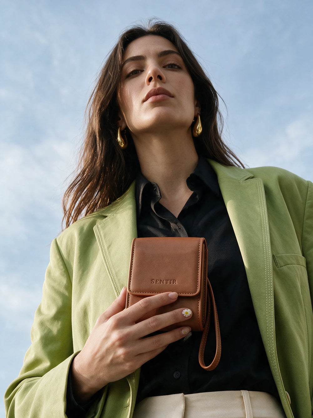 Woman in a green blazer holding the brown vegan leather Sentir travel pouch