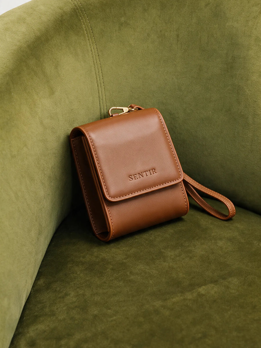 Brown vegan leather Sentir travel pouch resting on a green velvet chair